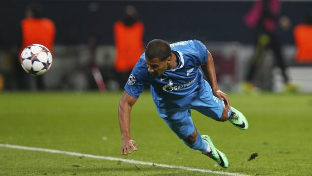 Ein Fußballspieler in blauem Trikot rutscht auf dem Rasen, während ein Fußball in der Luft ist.