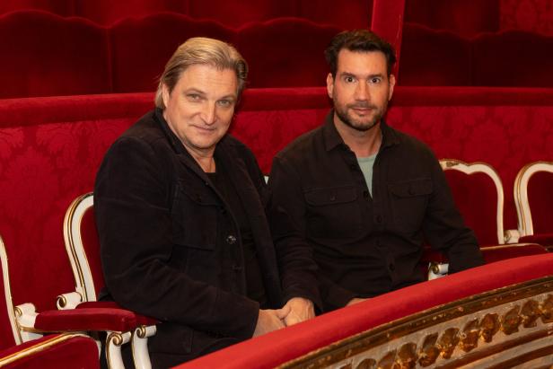 Zwei Männer sitzen in einem Theatersaal nebeneinander.