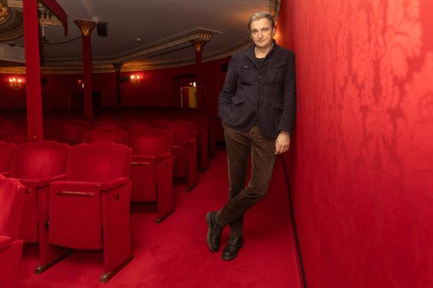 Ein Mann lehnt in einem roten Theatersaal an der Wand.