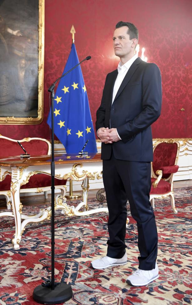 Ein Mann in Anzug steht vor der Europaflagge in einem eleganten Raum.