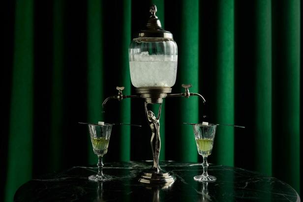 Ein Absinth-Brunnen tropft Wasser auf Zuckerwürfel über zwei Gläsern mit Absinth.