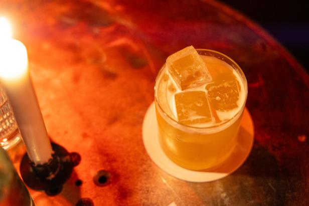 Ein Cocktail mit Eiswürfeln steht neben einer brennenden Kerze.