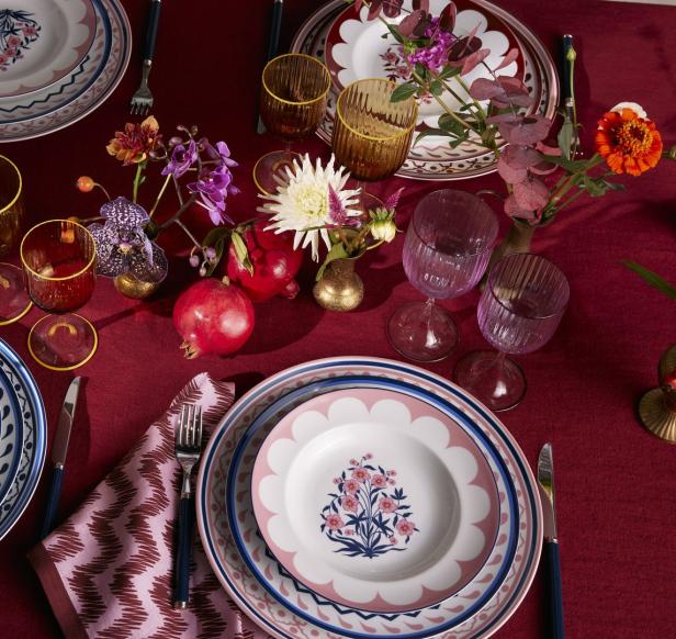 Ein festlich gedeckter Tisch mit Blumen, Tellern und Gläsern auf einer roten Tischdecke.