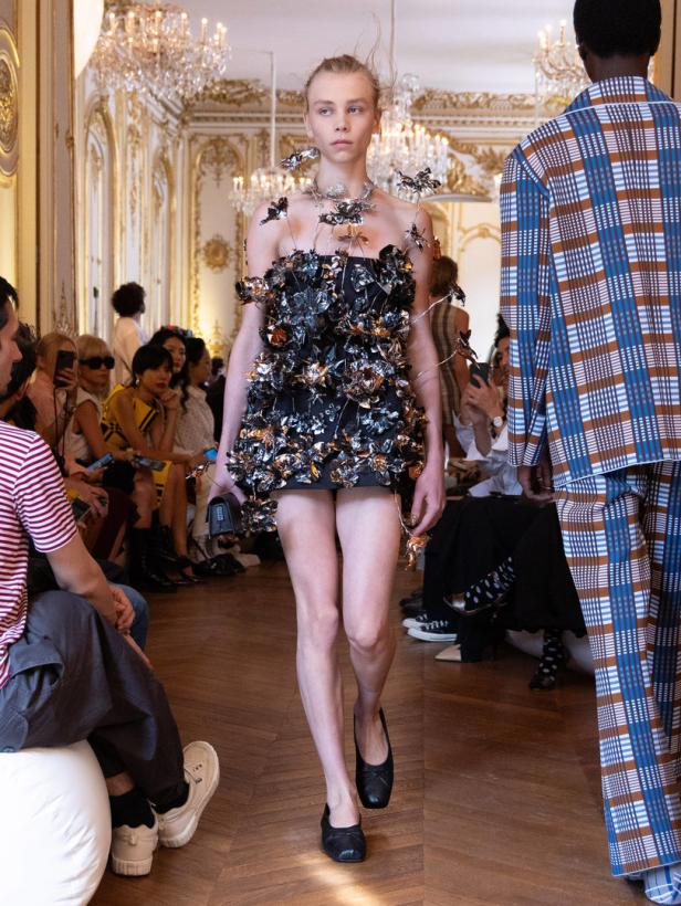 Ein Model präsentiert ein schwarzes, blumenverziertes Kleid auf dem Laufsteg.
