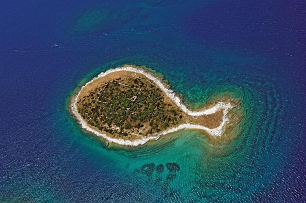 Eine kleine, bewaldete Insel mit Ruinen im türkisfarbenen Meer.