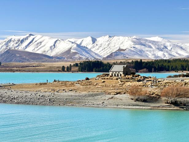 Die Church of the Good Shepherd am Ufer des türkisfarbenen Lake Tekapo vor schneebedeckten Bergen.