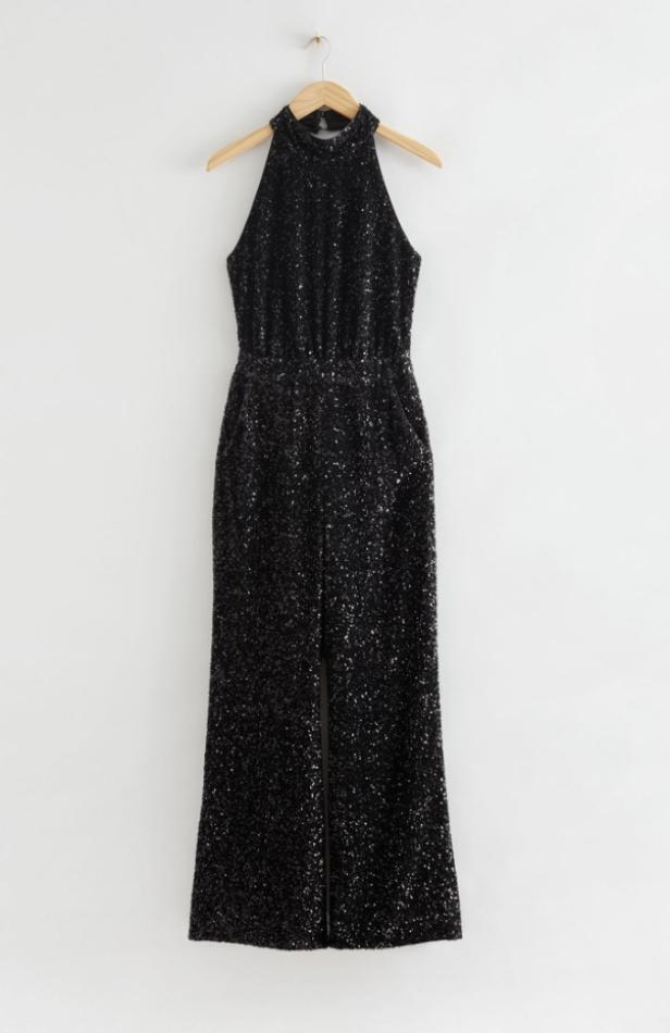 Ein schwarzer, glitzernder Jumpsuit hängt an einem Kleiderbügel.