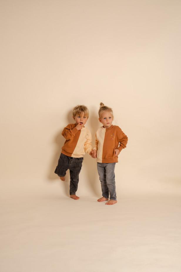 Ein Junge und ein Mädchen halten Händchen und tragen farblich abgesetzte Pullover.