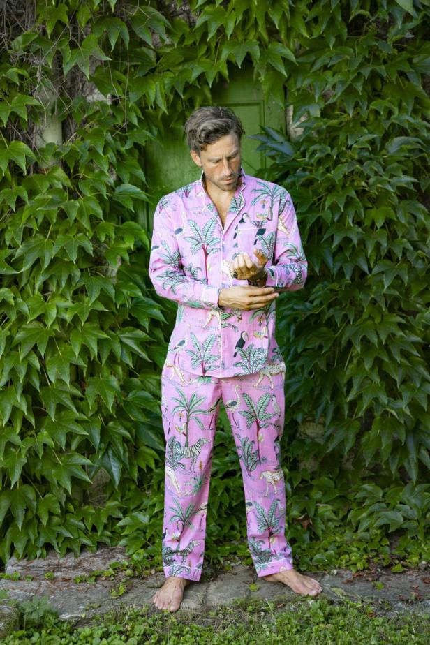 Ein Mann in einem rosa Pyjama mit Dschungelmotiven steht vor einer grünen Wand aus Efeu.