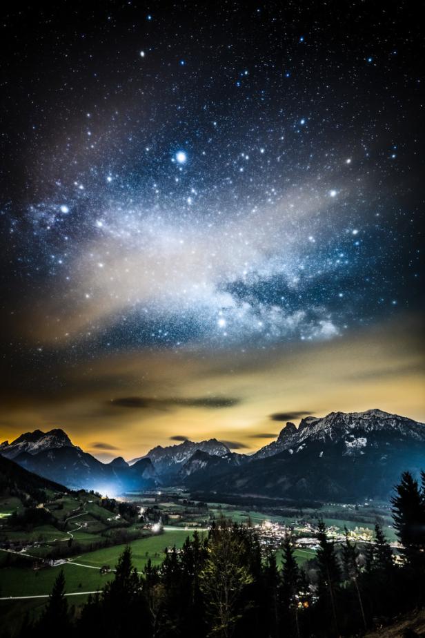 Sternenhimmel über einer Berglandschaft mit einer kleinen Stadt im Tal.