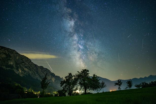 Die Milchstraße und Sternschnuppen über einer Berglandschaft.