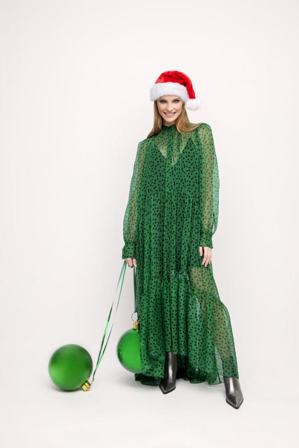 Eine Frau mit Weihnachtsmütze und grünem Kleid hält zwei übergroße Weihnachtskugeln.