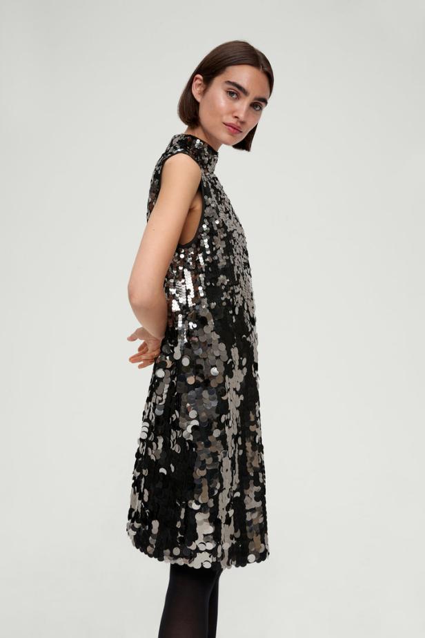 Eine Frau in einem ärmellosen, paillettenbesetzten Kleid mit Stehkragen.