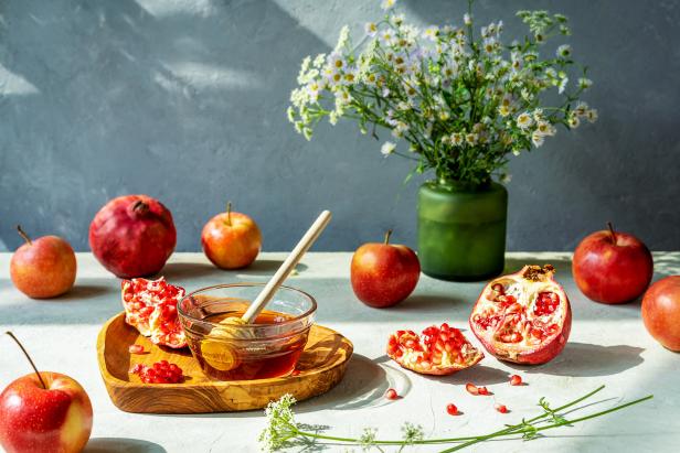 Äpfel vor weißem Hintergrund, Granatäpfel, Schale Honig, weiße Blumen in einer grünen Vase