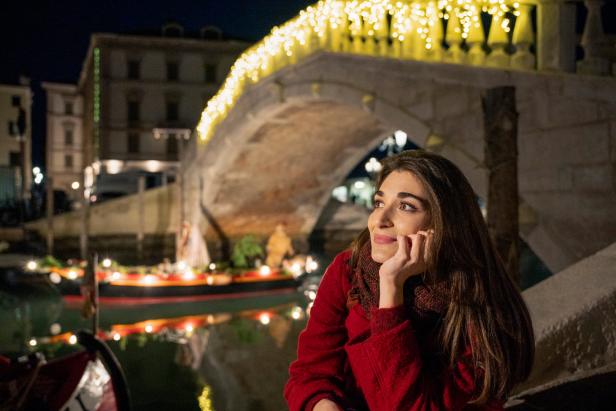 Eine Frau sitzt vor einer mit Lichtern geschmückten Brücke in Venedig.