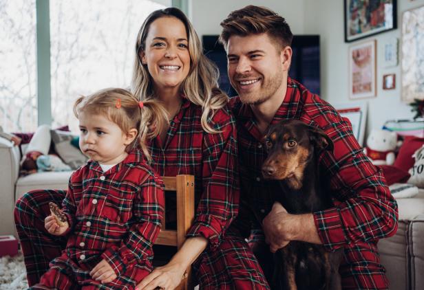 Eine Familie mit einem Hund trägt passende rot karierte Pyjamas und lächelt.