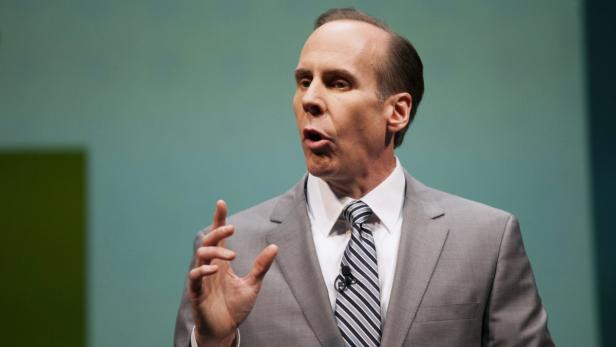 Ein Mann in einem grauen Anzug gestikuliert vor einem grünen Hintergrund.