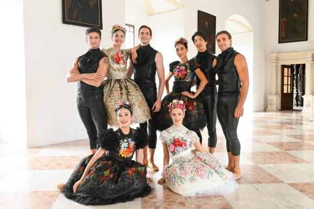 Eine Gruppe von Tänzern in farbenfrohen, traditionellen Kostümen posiert in einem eleganten Saal.