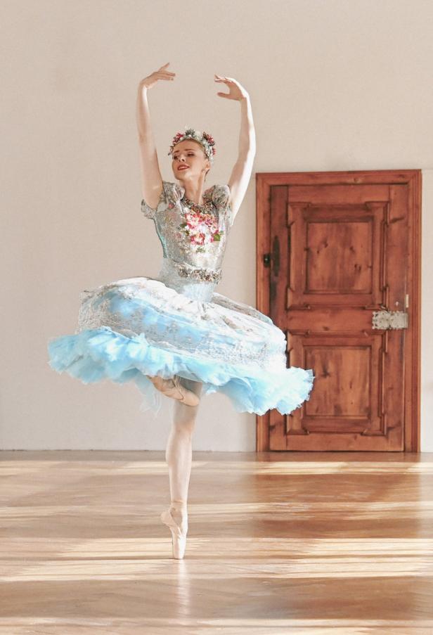 Eine Ballerina in einem verzierten Tutu und Spitzenschuhen posiert auf einem Bein.