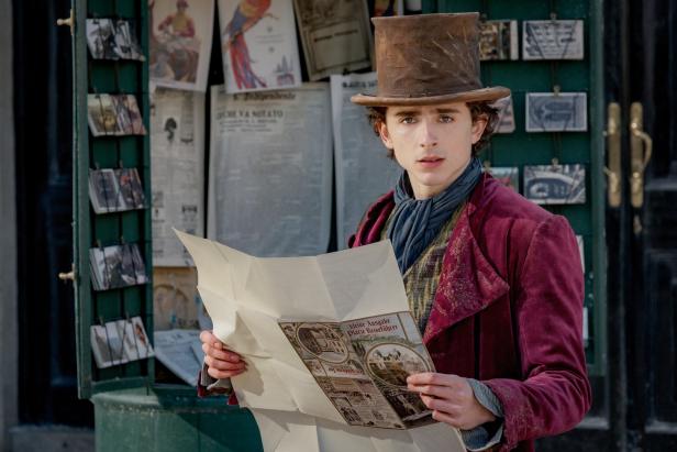Timothée Chalamet als Willy Wonka mit einem Reiseführer vor einem Zeitungsstand.