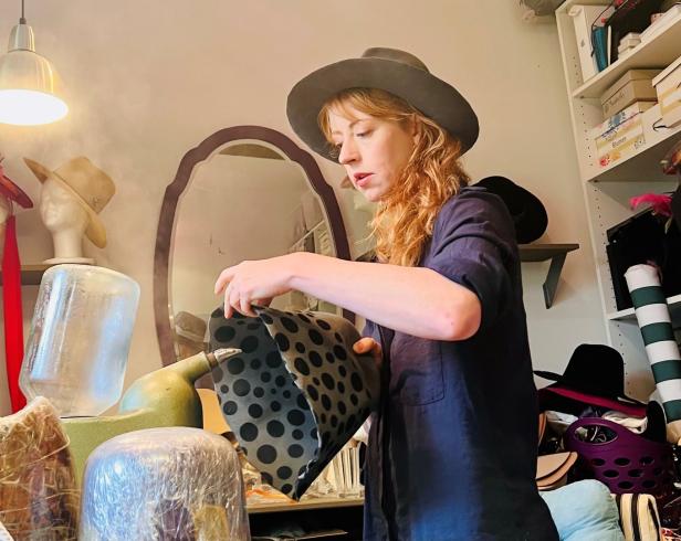 Eine Frau mit Hut hantiert mit einem gepunkteten Stoff in einem Atelier.
