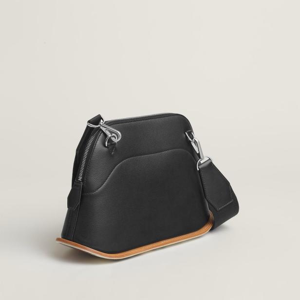 Eine schwarze Ledertasche mit einem Schultergurt vor einem neutralen Hintergrund.