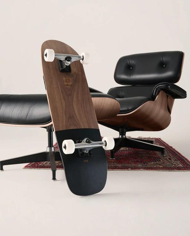 Ein Skateboard lehnt an einem schwarzen Ledersessel auf einem gemusterten Teppich.
