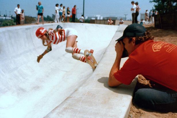 Eine Skateboardfahrerin stürzt in einer Halfpipe, während ein Fotograf sie aufnimmt.