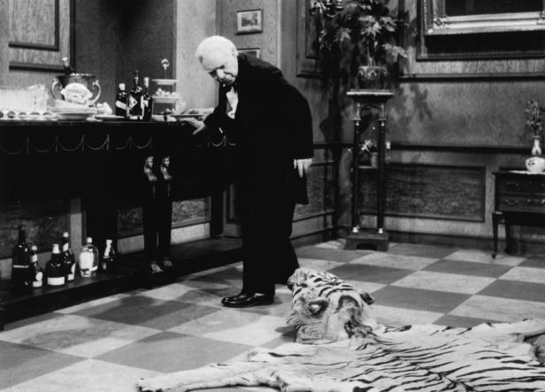 Ein Mann im Anzug steht neben einem Tigerfellteppich in einem eleganten Raum.