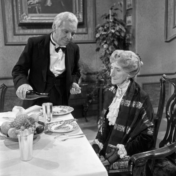 Ein Butler schenkt einer älteren Dame Wein ein.