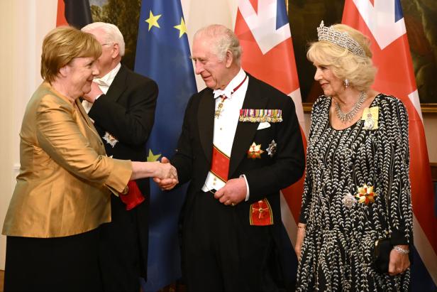 Angela Merkel schüttelt König Charles III. die Hand, während Königin Camilla daneben steht.