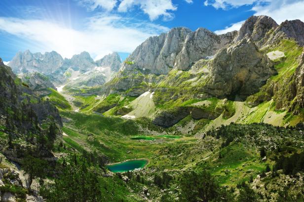 Blick auf grüne Berge und einen türkisfarbenen See unter blauem Himmel.