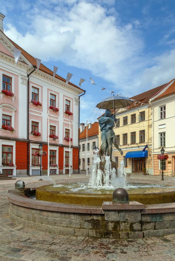 Fountain Kissing Students, Tartu, Estonia Ein Brunnen mit einer Skulptur eines Paares mit Regenschirm auf einem belebten Platz.