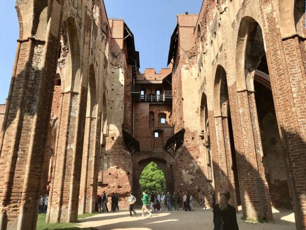 Alt-Livland Besucher erkunden die Ruinen einer alten Burg mit hohen Backsteinmauern und Bögen.