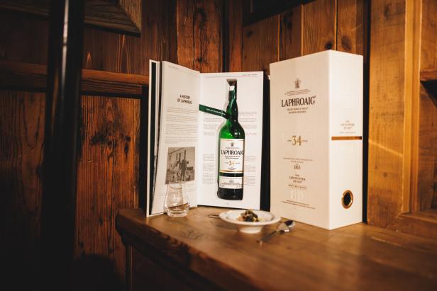 Eine Flasche Laphroaig 34 Jahre Single Malt Scotch Whisky mit Buch und Geschenkverpackung auf einem Holztisch.