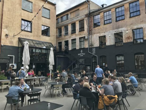 Gelände der Kreativhochburg Aparaaditehas Menschen sitzen im Freien vor dem Restaurant „Kolm Tilli“.