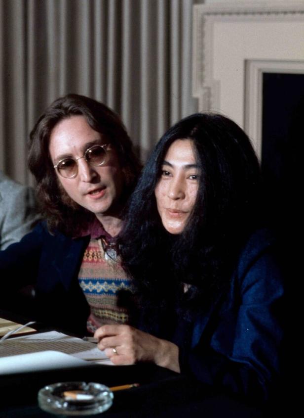 John Lennon und Yoko Ono sitzen an einem Tisch.