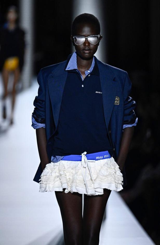 Ein Model präsentiert einen Preppy-Look mit Blazer, Poloshirt und Rüschenrock.