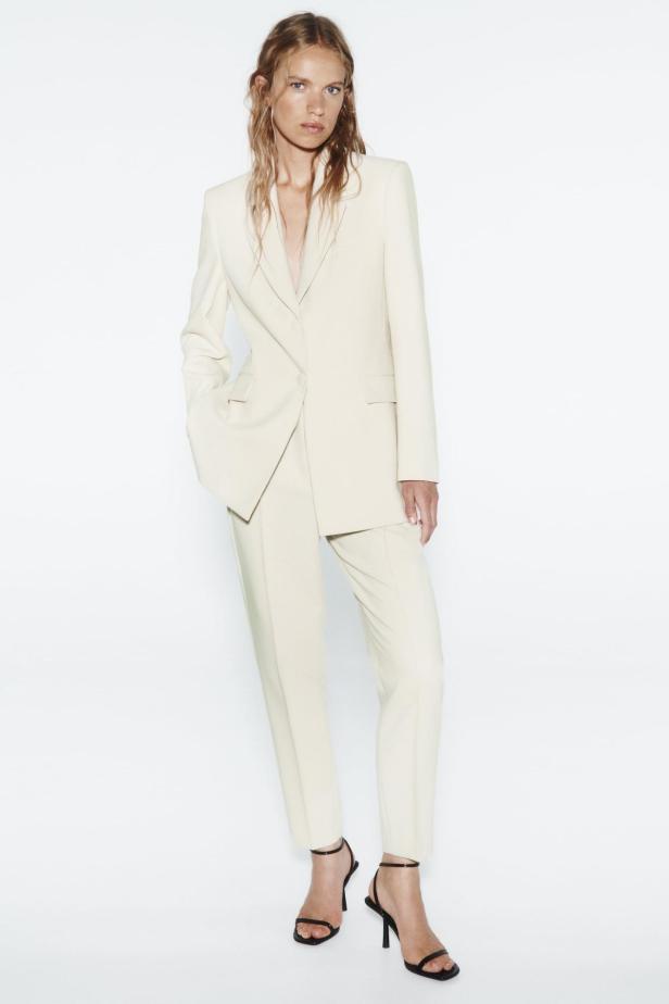 Eine Frau trägt einen weißen Blazer und eine passende Hose.