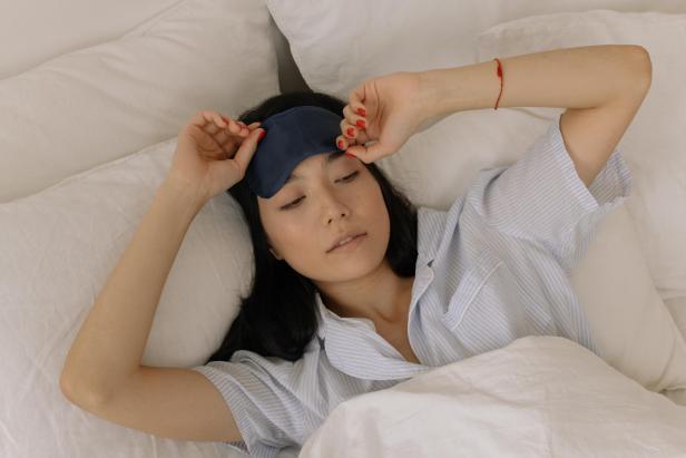 Eine Frau mit Schlafmaske liegt in einem weißen Bett.