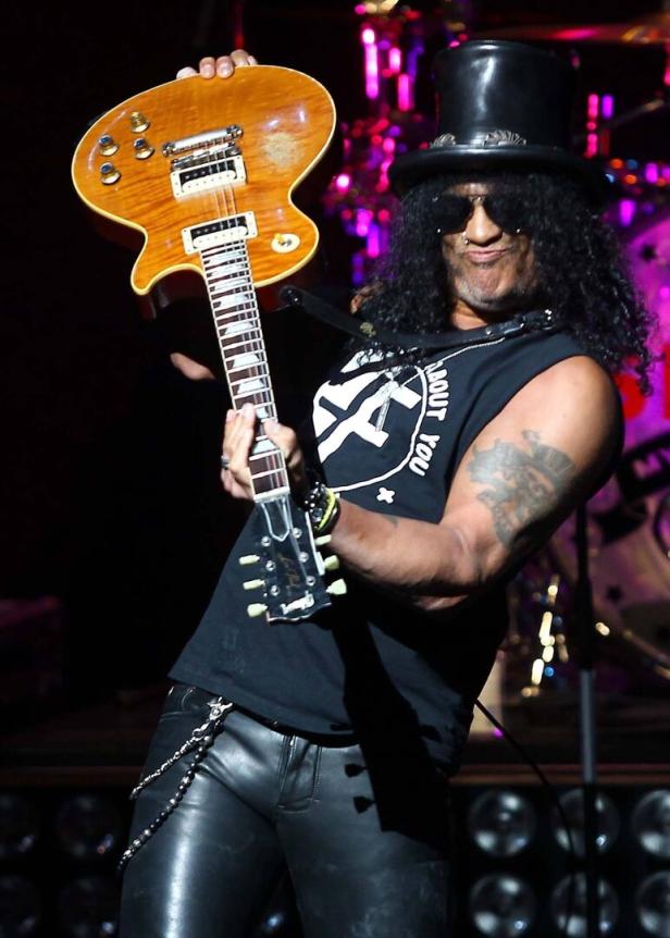 Slash mit Zylinder hält eine goldene Gitarre in die Höhe.