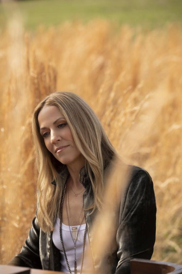 Sheryl Crow vor einem Feld mit hohem, goldenem Gras.