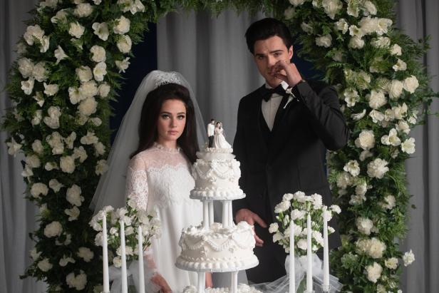 Ein Brautpaar steht an seiner Hochzeit vor einer Blumendekoration und einer Hochzeitstorte.