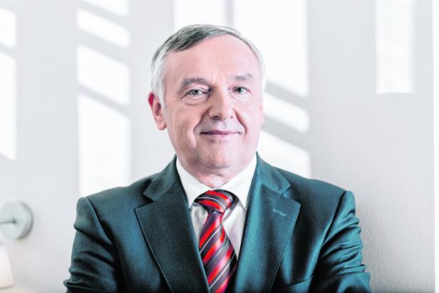 Ein älterer Mann mit Anzug und Krawatte lächelt in die Kamera.