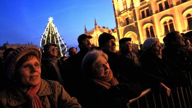 Eine Menschenmenge versammelt sich vor einem Weihnachtsbaum und einem Gebäude in der Abenddämmerung.