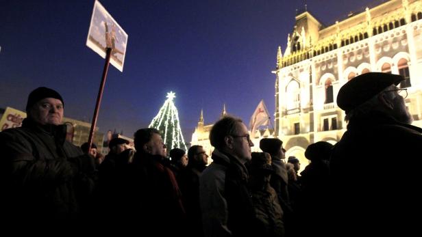 Eine Menschenmenge versammelt sich vor dem beleuchteten ungarischen Parlament und einem Weihnachtsbaum.