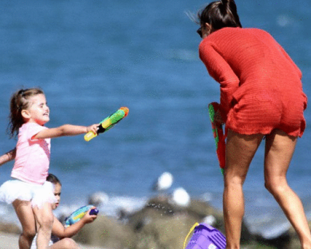 Eine Frau und zwei Kinder spielen am Strand mit Wasserpistolen.