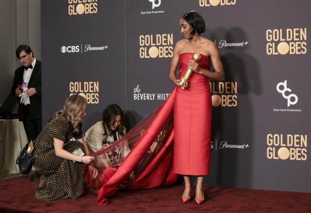 Eine Frau im roten Kleid hält einen Golden Globe Award, während ihr Kleid gerichtet wird.