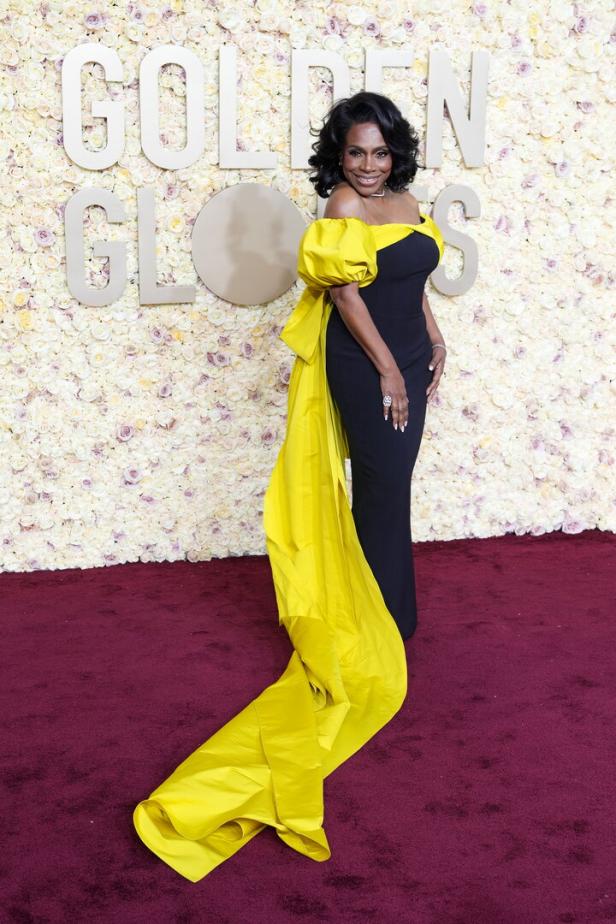 Eine Frau in einer schwarzen Robe mit gelben Akzenten posiert vor einer Blumenwand bei den Golden Globes.