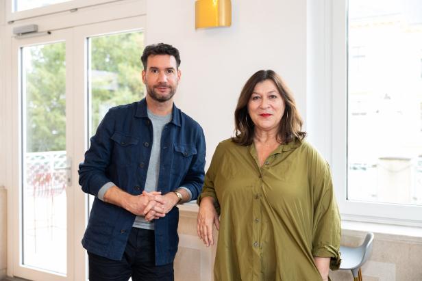 Ein Mann in Jeansjacke und eine Frau in olivgrüner Bluse posieren nebeneinander.